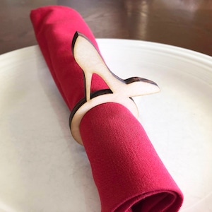 May include: A wooden napkin ring shaped like a high heel shoe. The ring is holding a red napkin.