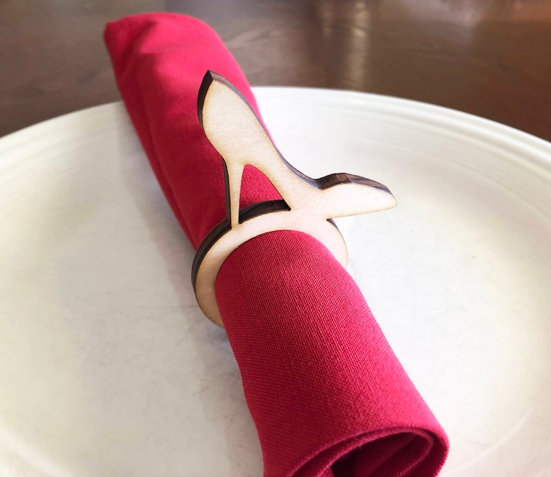 May include: A wooden napkin ring shaped like a high heel shoe. The ring is holding a red napkin.