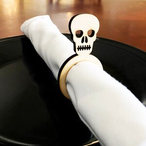 May include: A wooden napkin ring shaped like a skull with a white napkin. The skull is a light brown color and has a simple design.