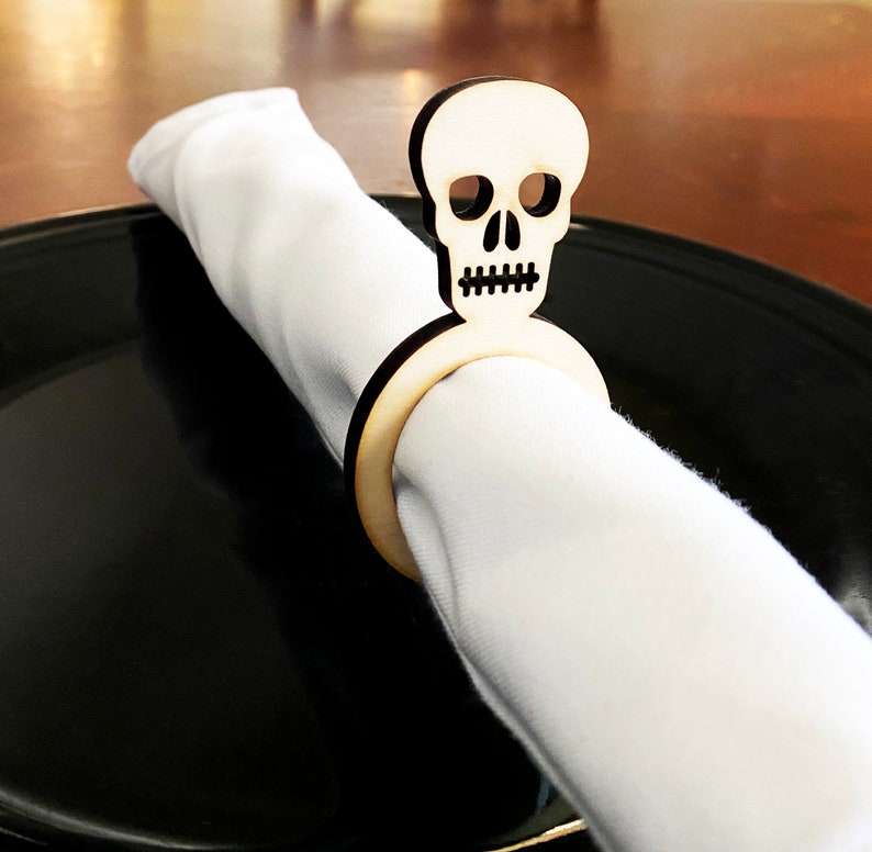 May include: A wooden napkin ring shaped like a skull with a white napkin. The skull is a light brown color and has a simple design.