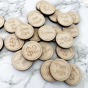 May include: A selection of circular wooden tokens, each engraved with different phrases and monetary values. Phrases include "Date with Mo," "Game Night," "New Book," "Surprise," "Go to the Park," and "Pizza Night." Values are £1, £2, and £5.