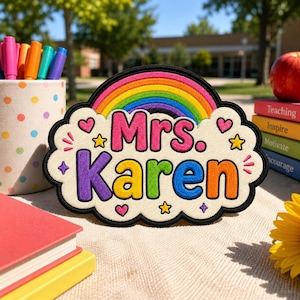 May include: A cloud-shaped embroidered patch featuring a rainbow at the top and the text Mrs. Karen in colourful letters. The design includes small embroidered hearts and stars on a cream-coloured background with a thick black border outline.