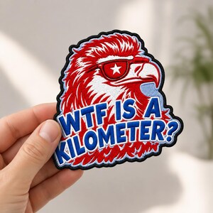 May include: An embroidered patch featuring a red, white, and blue eagle wearing sunglasses with a white star on the lens. The text "WTF IS A KILOMETER?" is stitched in bold blue letters across the bottom of the eagle design with a black border.