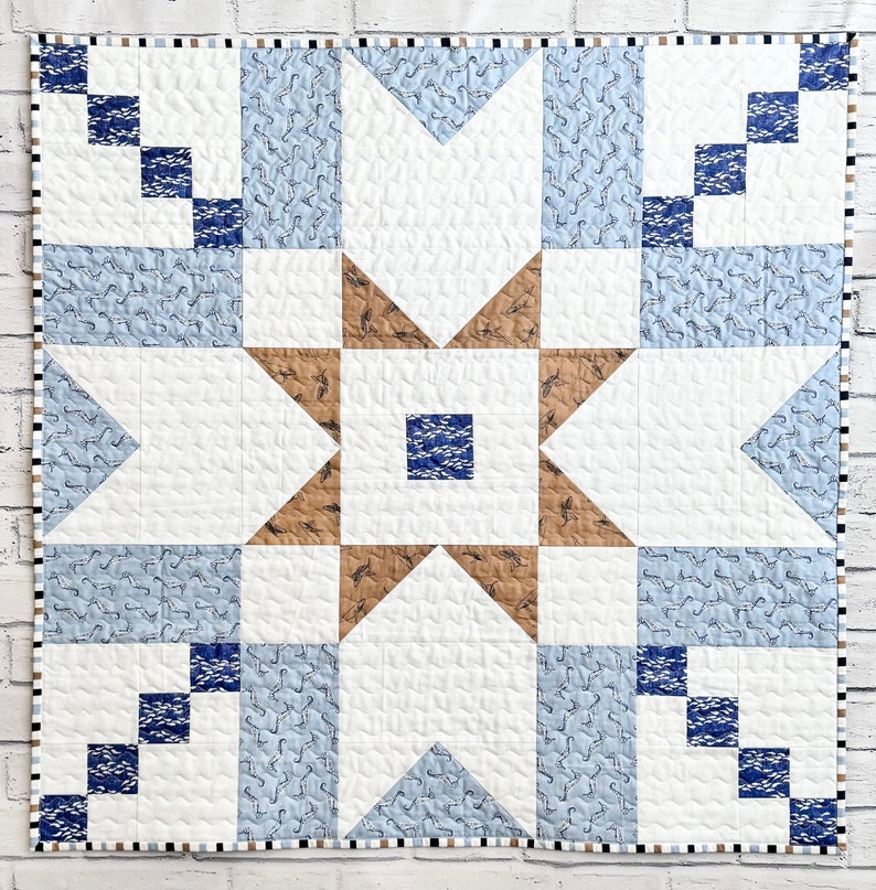 以下が含まれることがあります： 中央に星形のデザインが施された青と茶色のパッチワークキルト。キルトは、白の模様が入った青い生地と、白の模様が入った茶色の生地など、さまざまな生地で作られています。