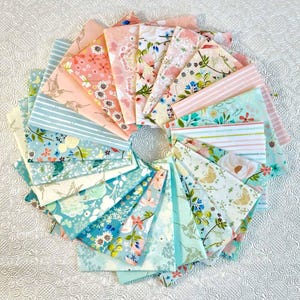 May include: A collection of 24 fabric squares featuring a variety of floral and bird patterns in shades of pink, blue, and white. The fabric squares are arranged in a fan shape, with the tips of the squares pointing towards the center.