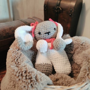 May include: A grey and white crocheted bunny toy with pink accents, sitting in a brown faux fur basket.