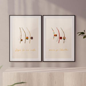Op de afbeelding: Twee ingelijste kunstprints met abstracte illustraties van capoeira-instrumenten. De prints hebben beige achtergronden met zwarte frames. Eén print heeft de tekst "Joga la na roda" in gouden script, de andere leest "para se libertar".