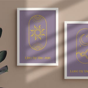Op de afbeelding: Twee ingelijste prints met een paarse achtergrond en gouden tekst. De eerste print toont een gestileerde zon met stralen en de tekst "Live by the sun". De tweede print toont een gestileerde maan met sterren en de tekst "Love by the moon".