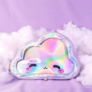 May include: A cloud-shaped purse with a holographic, iridescent front panel. The purse has a silver trim and a cartoon face with closed eyes and rosy cheeks. The background is a soft purple with fluffy white clouds.