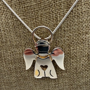 May include: A silver angel pendant necklace with a heart cutout. The angel has outstretched wings and a halo. The necklace chain is a thin, silver snake chain. The pendant is made of polished silver and gold-colored metal.