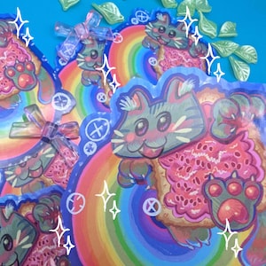 Puede incluir: Una colección de pegatinas coloridas con un diseño de gato de dibujos animados. El gato tiene pelaje gris y rosa, un fondo de arcoíris y una pata rosa. Las pegatinas tienen una estética caprichosa y juguetona, con un fondo azul.