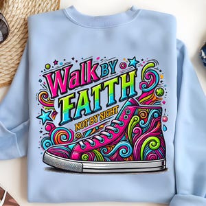 May include: Light blue sweatshirt featuring a colorful graphic of a high-top sneaker with the words "Walk by Faith Not by Sight." The sneaker design includes swirls and stars in pink, green, blue, and yellow. The text is in a bold, vibrant font.