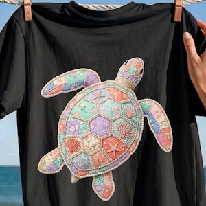 May include: A black t-shirt featuring a large, central graphic of a sea turtle. The turtle's shell and limbs are composed of a patchwork of pastel-colored floral and geometric patterns, outlined with a white beaded border and sea life motifs.