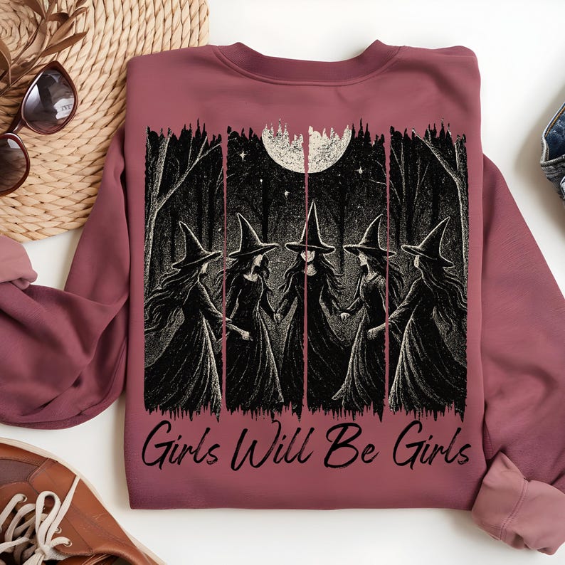May include: Mauve sweatshirt with a black and white graphic of five witches in a forest under a full moon. The text "Girls Will Be Girls" is printed below the graphic. The sweatshirt has long sleeves.