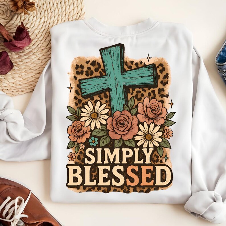 May include: White sweatshirt with a teal cross design, surrounded by flowers and a leopard print background. The words "SIMPLY BLESSED" are printed in a bold, vintage font. The sweatshirt is a comfortable, casual style.