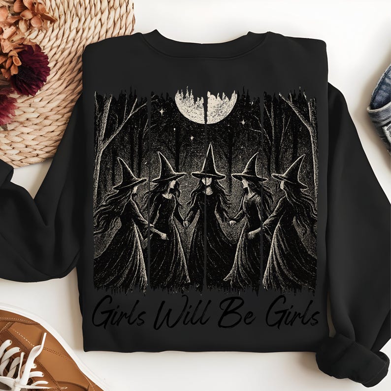 May include: Black sweatshirt with a graphic of five witches in a forest under a full moon. The words "Girls Will Be Girls" are printed in white. The design has a dark, gothic aesthetic, perfect for Halloween or alternative fashion.
