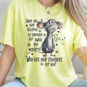 May include: A light yellow t-shirt featuring a cartoon mouse with the text "Have you ever listened to someone for awhile and wondered Who ties your shoelaces for you?" The mouse is gray and white.