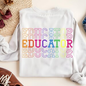 May include: White sweatshirt with the word "EDUCATOR" in a rainbow-colored, stacked design. The word is outlined in various colors, including orange, yellow, blue, and purple. The sweatshirt is made of a soft material.
