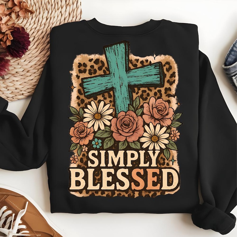 May include: Black sweatshirt featuring a turquoise cross, floral arrangement, and leopard print background. The words "SIMPLY BLESSED" are printed in a decorative font. The design includes roses, daisies, and other flowers.