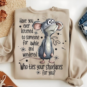May include: Beige sweatshirt featuring a cartoon mouse with large eyes, looking upwards. The text on the shirt reads: "Have you ever listened to someone for awhile and wondered, Who ties your shoelaces for you?" The design includes stars and dots.