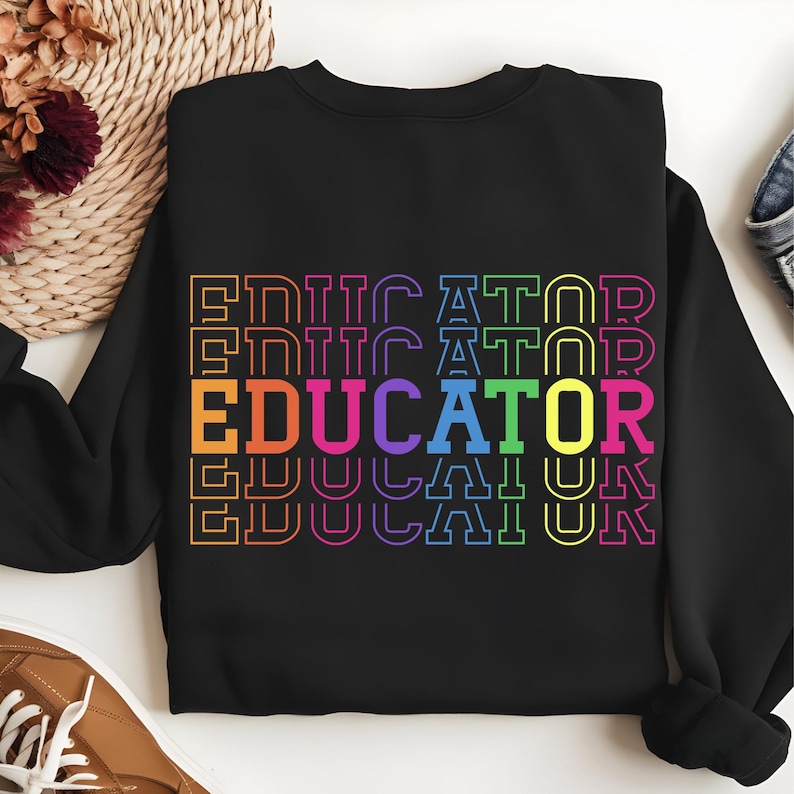 May include: Black sweatshirt with the word "EDUCATOR" in a stacked, rainbow-colored design. The word is outlined in a contrasting color, with each letter in a different hue. The sweatshirt is a casual garment.