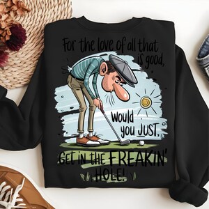 Puede incluir: Sudadera negra con un dise&ntilde;o de golf. El dise&ntilde;o presenta un golfista de dibujos animados con el texto "For the love of all that is good, Would you JUST GET IN THE FREAKIN' HOLE!"