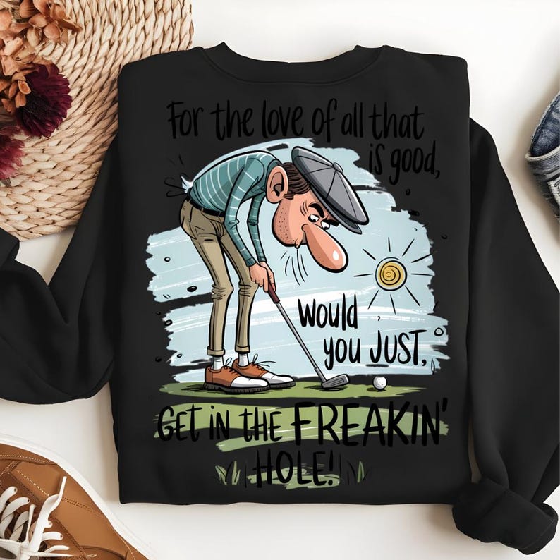 Puede incluir: Sudadera negra con un dise&ntilde;o de golf. El dise&ntilde;o presenta un golfista de dibujos animados con el texto "For the love of all that is good, Would you JUST GET IN THE FREAKIN' HOLE!"