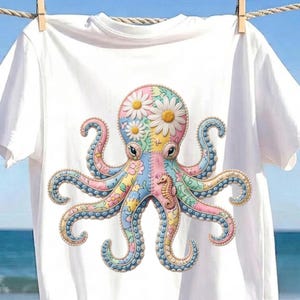 Op de afbeelding: Een wit T-shirt met korte mouwen en een grote, centrale afbeelding van een octopus. De octopus is ontworpen met een patchworkpatroon in pasteltinten, bloemmotieven, witte madeliefjes op de kop en een kleine afbeelding van een zeepaardje.