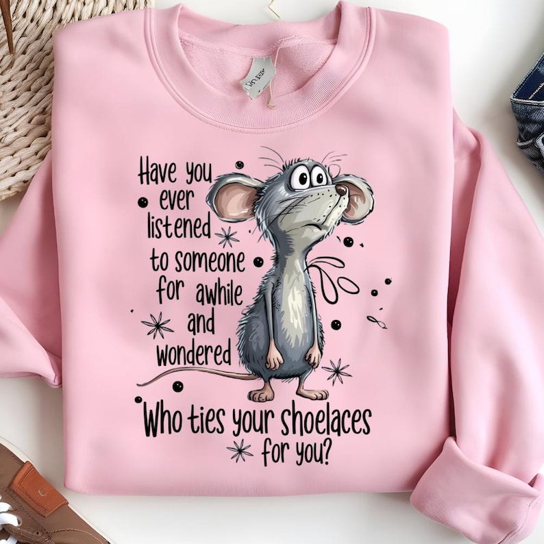 May include: Pink sweatshirt with a cartoon mouse illustration and the text "Have you ever listened to someone for awhile and wondered Who ties your shoelaces for you?" The mouse is gray with large ears and a curious expression.