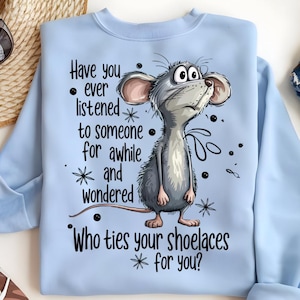 May include: Light blue sweatshirt featuring a cartoon mouse with large eyes and a questioning expression. The text on the shirt reads, "Have you ever listened to someone for awhile and wondered, Who ties your shoelaces for you?"