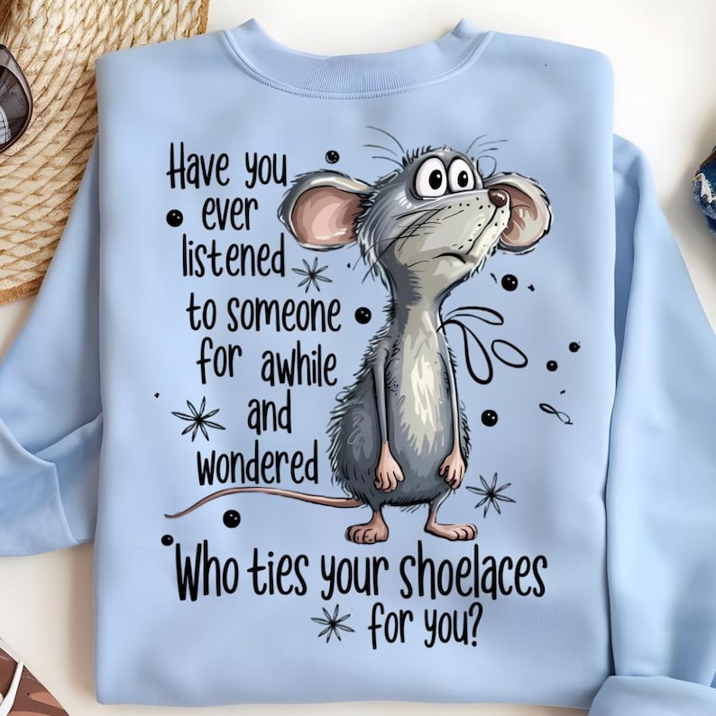 May include: Light blue sweatshirt featuring a cartoon mouse with large eyes and a questioning expression. The text on the shirt reads, "Have you ever listened to someone for awhile and wondered, Who ties your shoelaces for you?"