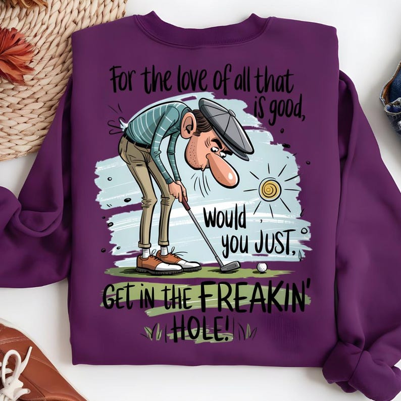 Puede incluir: Una sudadera morada con un dise&ntilde;o de golf. La ilustraci&oacute;n muestra a un golfista con el texto: "For the love of all that is good, Would you JUST, GET IN THE FREAKIN' HOLE!" Incluye una pelota de golf y un sol.