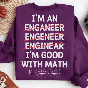 May include: A purple sweatshirt with white text that reads "I'M AN ENGINEER, I'M GOOD WITH MATH." The word "engineer" is crossed out three times. A mathematical formula is at the bottom. The sweatshirt is a crew neck style.