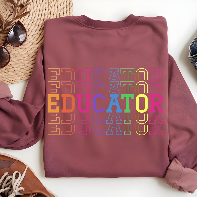 May include: A maroon sweatshirt with the word "EDUCATOR" in a rainbow of colors. The word is stacked vertically and repeated multiple times. The sweatshirt is made of a soft material.