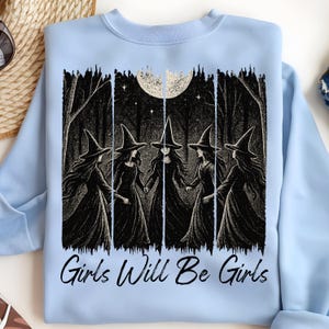May include: Pale blue sweatshirt with a black and white graphic of five witches in a forest, holding hands beneath a full moon. The words "Girls Will Be Girls" are printed below the image.