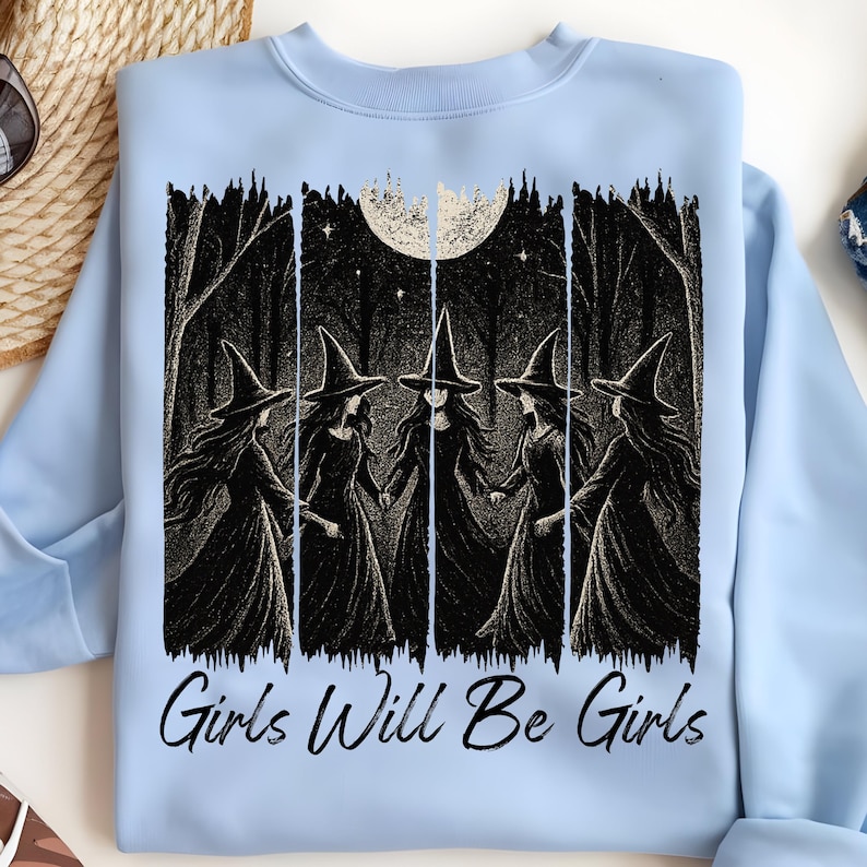 May include: Pale blue sweatshirt with a black and white graphic of five witches in a forest, holding hands beneath a full moon. The words "Girls Will Be Girls" are printed below the image.