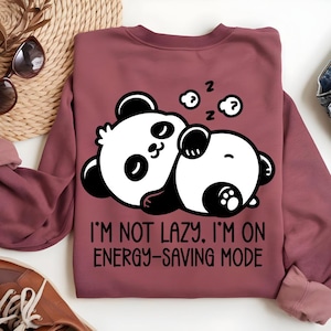 May include: A maroon sweatshirt featuring a graphic of two sleeping panda bears in black and white. The text "I'M NOT LAZY. I'M ON ENERGY-SAVING MODE" is printed below the pandas. The sweatshirt has long sleeves.