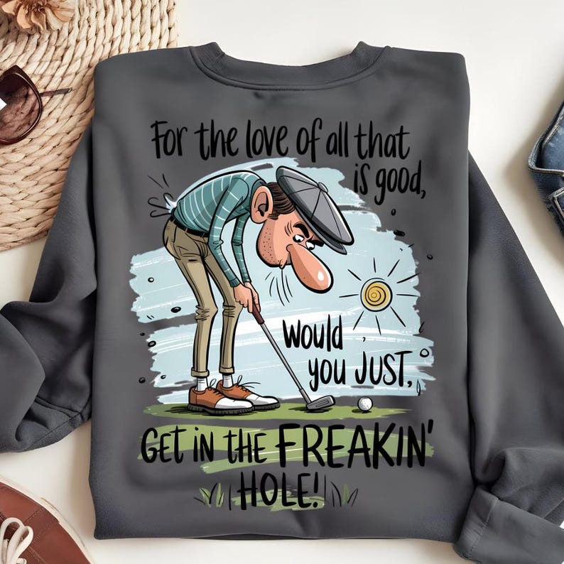 Puede incluir: Sudadera gris oscuro con un gr&aacute;fico humor&iacute;stico con tem&aacute;tica de golf. El dise&ntilde;o presenta un golfista de dibujos animados y el texto "For the love of all that is good, would you JUST, GET IN THE FREAKIN' HOLE!" en una fuente divertida.