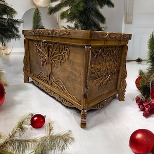 May include: A wooden storage chest with intricate carvings of a tree of life. The chest is brown and has a distressed finish. It has a hinged lid and decorative feet.
