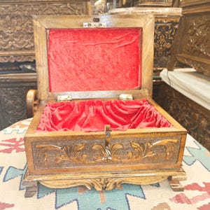 May include: A wooden box with intricate carvings and a red velvet lining. The box has a hinged lid and a brass lock.