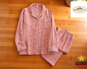 May include: Pink pajama set with a floral pattern. The set includes a long-sleeved button-down shirt with a chest pocket and matching pants. The pajamas have white trim and are made of a soft, lightweight fabric.