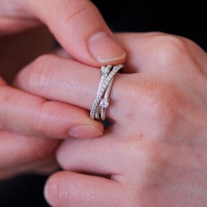 May include: A silver ring with multiple bands and small diamonds. The ring is worn on a person's finger.