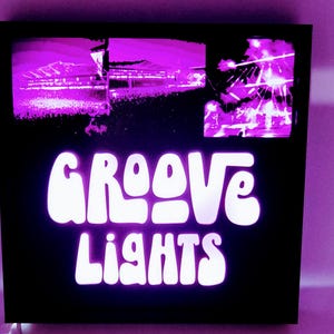 May include: A black framed sign with a white neon sign that reads "GROOVE LIGHTS". The sign has two images of a concert crowd in the background.