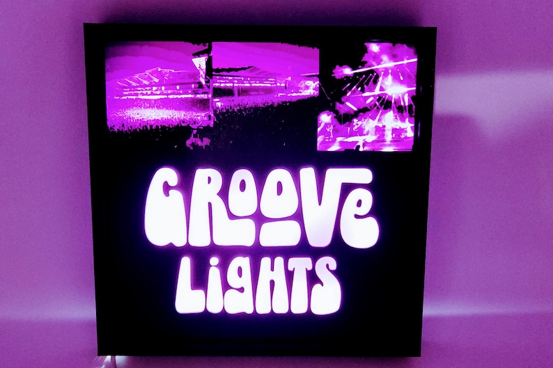 May include: A black framed sign with a white neon sign that reads "GROOVE LIGHTS". The sign has two images of a concert crowd in the background.