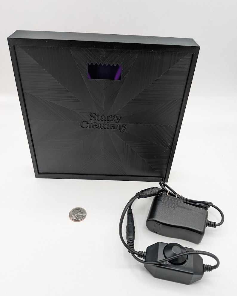 May include: A black square box with a purple light inside. The box has the text "Starzy Creations" on it. The box is connected to a black power adapter and a black dimmer switch.