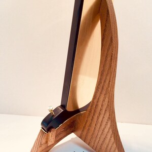 May include: A wooden stand with a curved design, supporting a black and gold framed object. The stand has a natural wood grain finish. The frame has a black border and a gold interior.