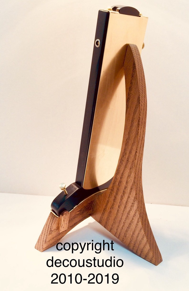 May include: A wooden stand with a curved design, supporting a black and gold framed object. The stand has a natural wood grain finish. The frame has a black border and a gold interior.