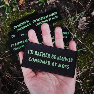 Könnte beinhalten: Ein schwarzer Patch mit grünem Text, der "Ich würde lieber langsam von Moos gefressen werden" lautet.