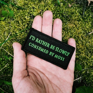 Könnte beinhalten: Ein schwarzer Patch mit grünem Text, der "Ich würde lieber langsam von Moos gefressen werden" lautet.