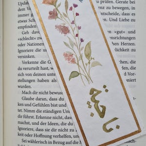 May include: A watercolour illustration of a floral bouquet with a gold border and the number "1" in the top right corner. The text "Mach dir nicht bewusst" is visible in the lower left corner.